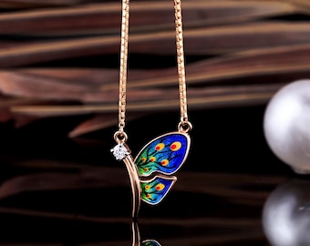 May include: A gold chain necklace with a butterfly pendant. The butterfly is blue, green, and yellow with red accents. A small diamond is set in the center of the butterfly.