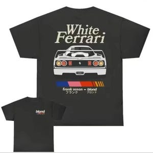 K&ouml;nnte beinhalten: Schwarzes T-Shirt mit einer wei&szlig;en Grafik eines Ferrari und dem Text "White Ferrari" dar&uuml;ber. Unter dem Auto steht der Text "frank ocean - blond" in einem gestreiften Design. Ein kleineres T-Shirt mit dem Wort "blond" ist ebenfalls sichtbar.
