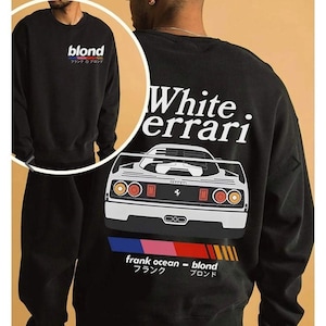 K&ouml;nnte beinhalten: Schwarzes Sweatshirt mit dem Wort "blond" und japanischen Schriftzeichen auf der Vorderseite. Auf der R&uuml;ckseite befindet sich eine wei&szlig;e Ferrari-Grafik, der Text "White. errari", "frank ocean - blond", japanischer Text und ein Farbbalken.