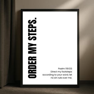 Op de afbeelding: Zwart omkaderde wandkunst met de tekst "ORDER MY STEPS" in een vetgedrukte, verticale lettertype. Daaronder staat "Psalm 119:133" gevolgd door een bijbelvers. Het kunstwerk staat tegen een witte achtergrond.