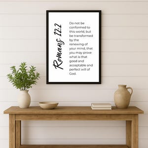 May include: A framed print with the text "Romans 12:2" in a script font. The print contains a quote about renewing the mind. The print is displayed on a wooden table with a vase and decorative items.