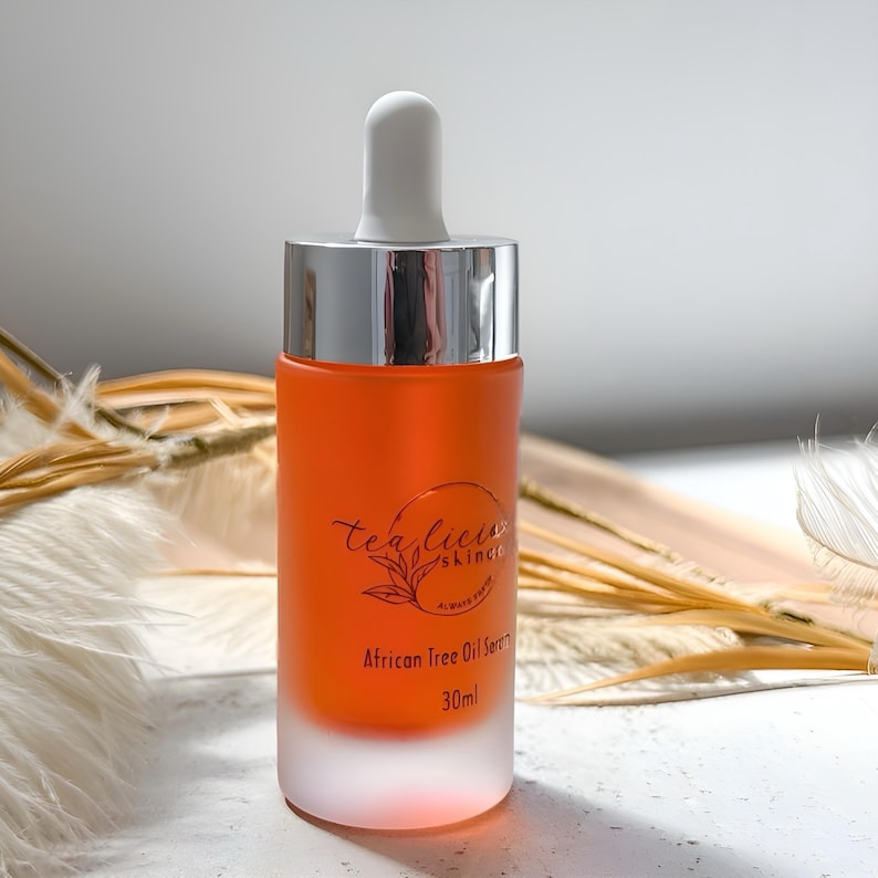 May include: A clear glass bottle with a frosted bottom and a silver cap. The bottle contains a bright orange liquid and has a dropper top. The bottle is labeled "tea tree skinco" and "African Tree Oil Serum 30ml".