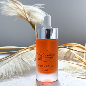 May include: A clear glass bottle with a silver cap and a dropper. The bottle contains a light orange liquid and has a label that reads "TeaLicious Skincare" and "African Free Oil Serum 30ml".