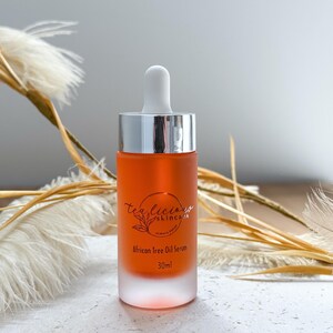 May include: A clear glass bottle with a silver cap and dropper, filled with a light orange liquid. The bottle is labeled "Tea Tree Skincare" and "African Tree Oil Serum 30 ml".