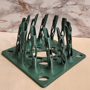 May include: A dark green 3D printed square rack featuring a series of vertical, hollow, organic-shaped pillars with oval cutouts. The base is a flat square plate with circular holes integrated into the design, creating a structured grid pattern.