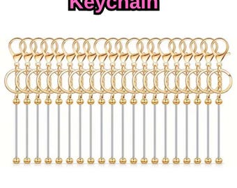 May include: A collection of gold-colored keychains with clear bars and gold ball accents. The keychains have a lobster clasp and a ring. Text at the top reads "Beadable Bar Blank Keychain". The Mama Crafts logo is at the bottom.