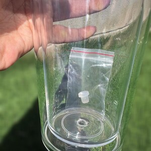 Pode incluir: Um copo de pl&aacute;stico transparente com uma tampa de pl&aacute;stico branco dentro de um saco de pl&aacute;stico transparente. O saco &eacute; selado com um fecho de correr vermelho.