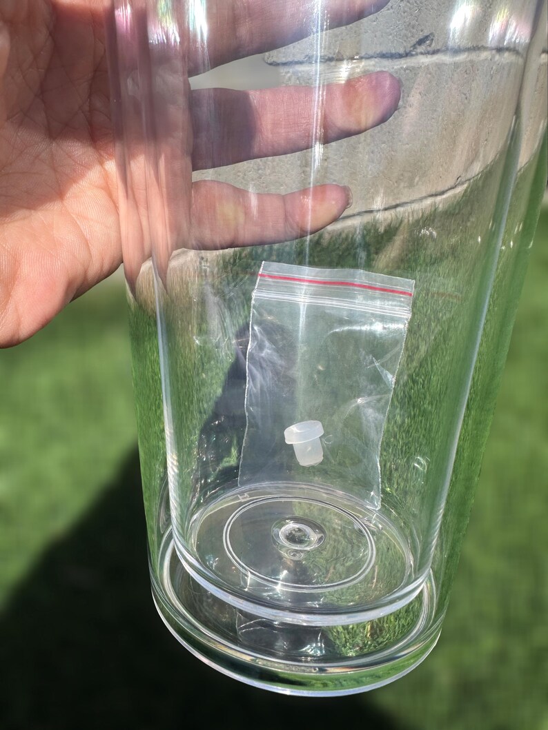 Pode incluir: Um copo de pl&aacute;stico transparente com uma tampa de pl&aacute;stico branco dentro de um saco de pl&aacute;stico transparente. O saco &eacute; selado com um fecho de correr vermelho.