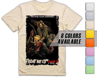 Puede incluir: Camiseta beige con un gráfico de "Friday the 13th Part II". El diseño muestra una escena de terror con el texto "The body count continues..." y "Friday the 13th Part II". La camiseta también muestra "8 COLORS AVAILABLE" en un recuadro.