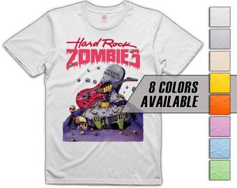 May include: White t-shirt featuring the text "Hard Rock Zombies" in red, with a graphic of a zombie playing a red guitar. The design includes a tombstone and green zombie hands. "8 Colors Available" is also displayed.