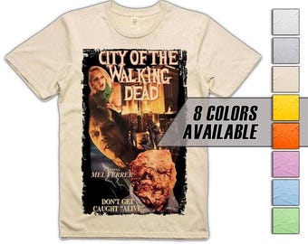Puede incluir: Camiseta beige con un diseño de cartel de película de "City of the Walking Dead". El gráfico incluye imágenes de actores y el texto "Don't Get Caught Alive". Hay ocho opciones de color disponibles.