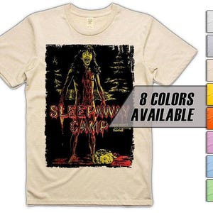 以下が含まれることがあります： ベージュ色のTシャツ。ホラー映画「Sleepaway Camp」のグラフィックがプリントされています。血まみれの人物が描かれ、映画タイトルは赤色で表示されています。「8 COLORS AVAILABLE」の文字も表示されています。シャツは明るい色です。