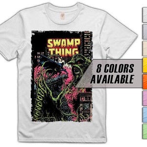 Puede incluir: Camiseta blanca con un estampado gráfico de Swamp Thing sobre un paisaje urbano. El diseño incluye el texto "SWAMP THING" en amarillo y negro. Una guía de colores indica "8 COLORES DISPONIBLES".