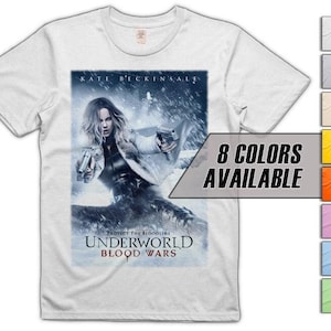 Puede incluir: Camiseta blanca con un gráfico de cartel de película. El cartel muestra a una mujer con dos pistolas, el texto "UNDERWORLD BLOOD WARS" y "8 COLORES DISPONIBLES".