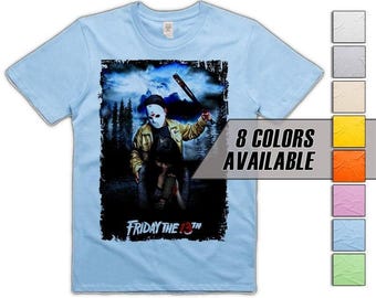 Könnte beinhalten: Hellblaues T-Shirt mit einem Grafikmotiv aus dem Horrorfilm "Freitag der 13.". Das Design zeigt eine maskierte Figur mit einer Waffe, der Filmtitel steht unten. Der Text "8 FARBEN VERFÜGBAR" wird ebenfalls angezeigt.