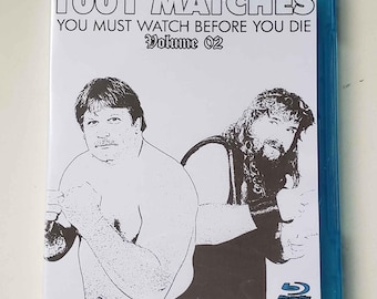 May include: A blue Blu-ray disc case with a white label. The label has the text "1001 Matches You Must Watch Before You Die Volume 02" and a black and white illustration of two wrestlers.