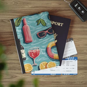 May include: A passport holder with a colorful design featuring a glass of wine, a bottle of wine, a pool float, and lemons. The design is on a blue background with white waves. The passport holder is made of leather and has a black border.