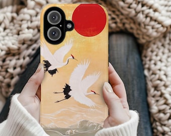 May include: A phone case with a design of two white cranes flying against a yellow background with a red sun. The case has a black camera lens cutout.