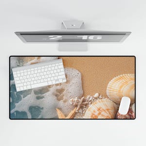 May include: A white computer keyboard and a white computer mouse are on a beach-themed mouse mat. The mouse mat features a sandy beach with white waves, seashells, and a starfish.