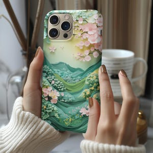May include: A green and pink phone case with a floral design and a mountain landscape. The case features a detailed paper cut-out style.