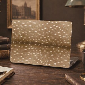 May include: A laptop skin featuring a realistic brown fur pattern with white spots, mimicking the appearance of a fawn's coat. The design covers the entire outer lid of the laptop, displaying a dense texture of short hair and a horizontal darker stripe.