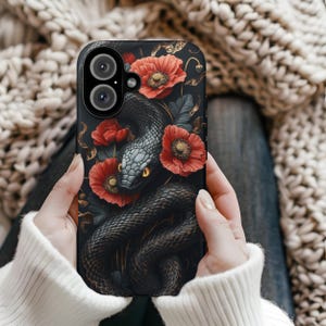 May include: Black phone case featuring a dark snake entwined around red poppies. The snake has yellow eyes and the phone case has a camera lens cutout.