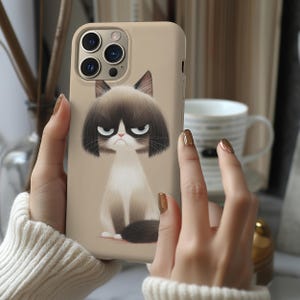 May include: Beige phone case featuring a cartoon illustration of a grumpy cat with a dark brown bob haircut and a white chest. The cat has a stern expression with furrowed eyebrows. The case has a matte finish and is held by a person.