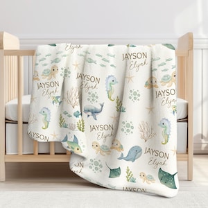 Peut inclure: Une couverture de bébé blanche sur le thème de l'océan, avec des illustrations d'hippocampes, de tortues, de baleines et de raies pastenagues dans des tons aquarelles doux. La couverture est personnalisée avec les noms "Jayson" et "Elyah".