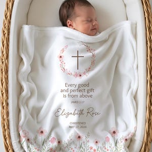 May include: A white baby blanket featuring a brown cross inside a pink floral wreath. The text reads: Every good and perfect gift is from above, JAMES 1:17, Elizabeth Rose, CHRISTENED MAY 17, 2026. The bottom edge has a pink and green floral print.