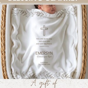 K&ouml;nnte beinhalten: Eine wei&szlig;e Baby-Segensdecke mit Kreuz- und Blumendesign, personalisiert mit Namen und Taufdatum. Die Decke liegt in einem Weidenkorb, mit dem Text "Personalized Baby Blessing Blanket".
