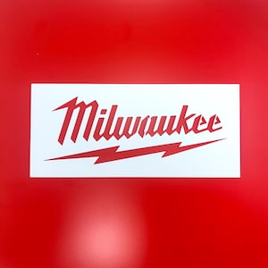 Puede incluir: Una pegatina rectangular blanca con la palabra "Milwaukee" en rojo, con un diseño de rayo rojo debajo. La pegatina está sobre un fondo rojo brillante.