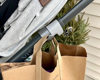 May include: A gray stroller with a brown paper bag hanging from the handle. The bag has the word "VISA" printed on it and the text "PLEASE HOLD BOTH HANDLES" on the bottom.