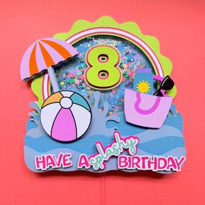 May include: A layered paper cake topper featuring a shaker element with the number 8, a beach umbrella, a beach ball, and a tote bag with sunglasses. The text reads HAVE A splashy BIRTHDAY in pink and teal, set against a blue water-themed base.