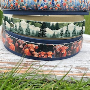K&ouml;nnte beinhalten: Drei verschiedene Hundehalsb&auml;nder mit bunten Designs. Das obere Halsband hat einen blauen Hintergrund mit einem floralen Muster aus orangefarbenen und blauen Blumen. Das mittlere Halsband hat einen beigefarbenen Hintergrund mit einer Waldszene aus gr&uuml;nen B&auml;umen und wei&szlig;en schneebedeckten Bergen. Das untere Halsband hat einen blauen Hintergrund mit einem Muster aus braunen und wei&szlig;en Highland-K&uuml;hen.