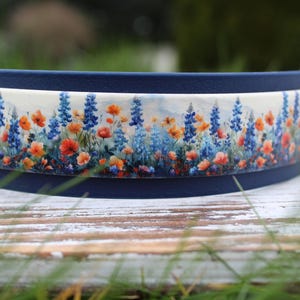 K&ouml;nnte beinhalten: Ein blaues und wei&szlig;es Halsband mit einem floralen Muster mit blauen, orangefarbenen und wei&szlig;en Blumen. Das Halsband ist aus strapazierf&auml;higem Material und f&uuml;r Hunde geeignet.