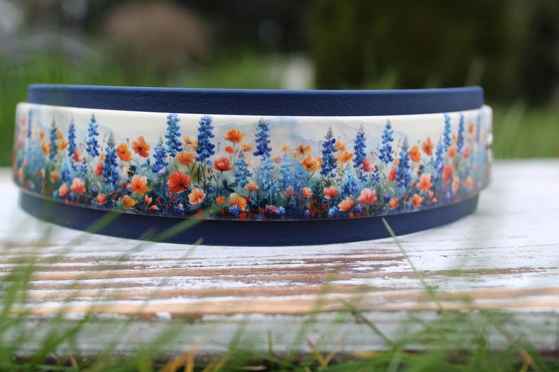 K&ouml;nnte beinhalten: Ein blaues und wei&szlig;es Halsband mit einem floralen Muster mit blauen, orangefarbenen und wei&szlig;en Blumen. Das Halsband ist aus strapazierf&auml;higem Material und f&uuml;r Hunde geeignet.