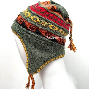 Puede incluir: Un gorro de punto verde con un colorido diseño geométrico en rojo, naranja y amarillo. El gorro tiene orejeras y borlas trenzadas con detalles en naranja y amarillo. El texto "Andean Hats" es visible.