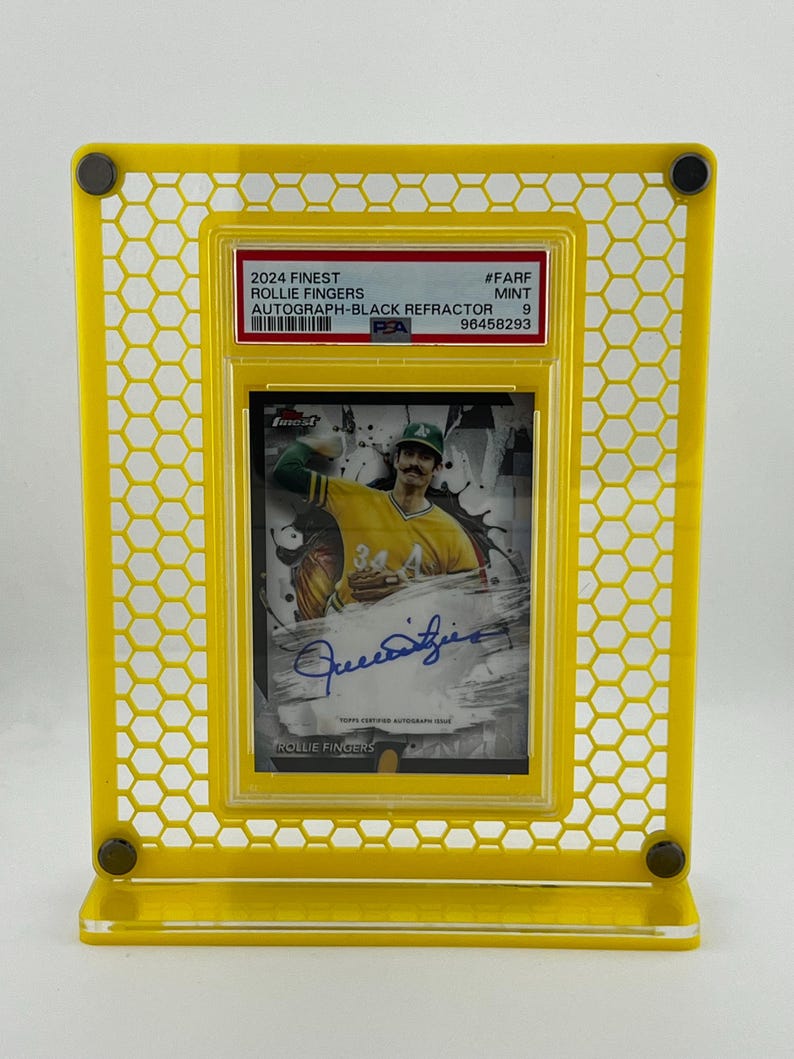 Puede incluir: Un expositor amarillo que contiene una tarjeta de b&eacute;isbol. La tarjeta presenta una imagen de Rollie Fingers, un aut&oacute;grafo y el texto "2024 Finest". El expositor tiene un patr&oacute;n de panal y est&aacute; hecho de un material transparente.