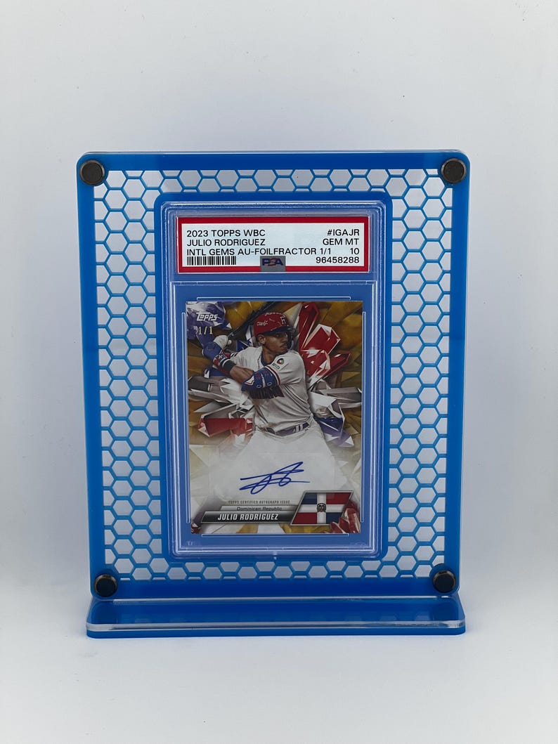 Puede incluir: Una tarjeta de b&eacute;isbol de Julio Rodr&iacute;guez, exhibida en un marco acr&iacute;lico azul. La tarjeta es de la serie 2023 Topps WBC, calificada como GEM MT 10. La tarjeta es una Intl Gems Au-Foilfractor 1/1.