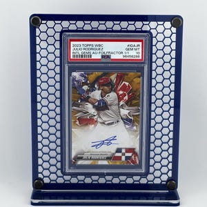 Puede incluir: Una tarjeta de b&eacute;isbol de Julio Rodr&iacute;guez, exhibida en un marco hexagonal azul. La tarjeta est&aacute; calificada e incluye el texto: "2023 Topps WBC Julio Rodr&iacute;guez Intl Gems Au-FoilFractor 1/1". La tarjeta tiene una imagen de Rodr&iacute;guez en acci&oacute;n.