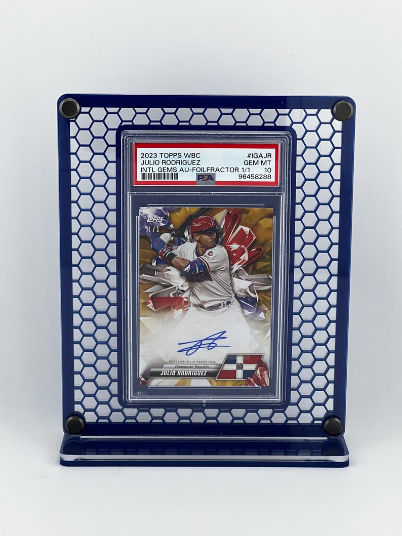 Puede incluir: Una tarjeta de b&eacute;isbol de Julio Rodr&iacute;guez, exhibida en un marco hexagonal azul. La tarjeta est&aacute; calificada e incluye el texto: "2023 Topps WBC Julio Rodr&iacute;guez Intl Gems Au-FoilFractor 1/1". La tarjeta tiene una imagen de Rodr&iacute;guez en acci&oacute;n.