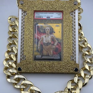 May include: A gold-colored chain necklace surrounds a gold glitter-framed Star Wars trading card featuring C-3PO. The card is graded and labeled with text including "2024 Star Wars Chrome" and "Aurebesh Var-Gold Ref".