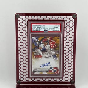 Puede incluir: Una tarjeta de b&eacute;isbol de Julio Rodr&iacute;guez, calificada y enmarcada, exhibida en un marco de metal burdeos. La tarjeta presenta una foto del jugador en acci&oacute;n, con el texto "2023 TOPPS WBC JULIO RODRIGUEZ". El marco tiene un dise&ntilde;o de panal.