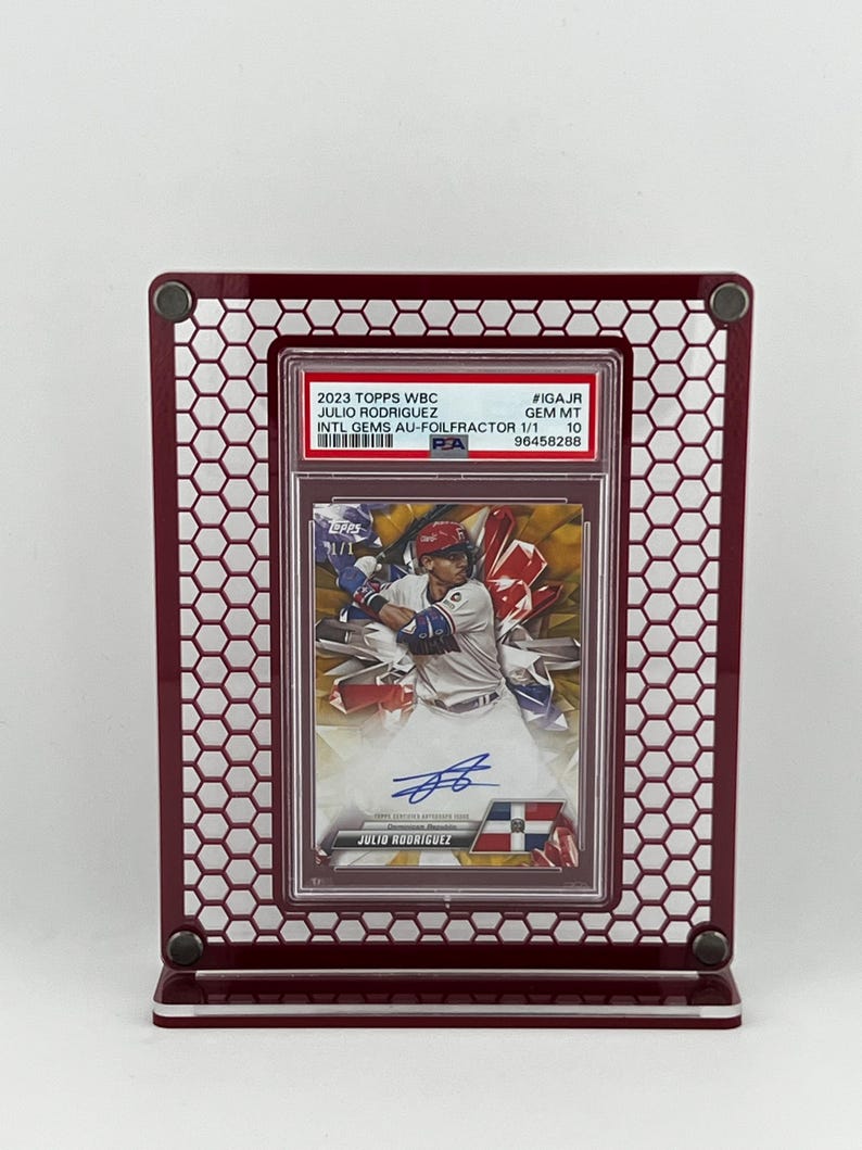 Puede incluir: Una tarjeta de b&eacute;isbol de Julio Rodr&iacute;guez, calificada y enmarcada, exhibida en un marco de metal burdeos. La tarjeta presenta una foto del jugador en acci&oacute;n, con el texto "2023 TOPPS WBC JULIO RODRIGUEZ". El marco tiene un dise&ntilde;o de panal.
