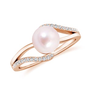 May include: Rose gold ring with a large, round, pale pink pearl at its centre. The band splits into two curving arms, each set with small, sparkling clear stones. The ring is displayed against a white background.