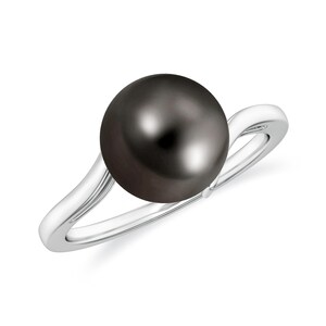 Puede incluir: Un anillo de plata con una perla grande, brillante y de color gris oscuro. La banda del anillo tiene un diseño suave y fluido que se curva hacia arriba para sostener la perla. La perla es perfectamente redonda y refleja la luz.
