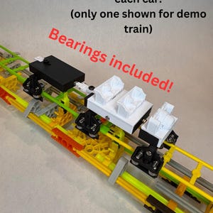 May include: A model train track with three cars. The track is made of yellow, green, and orange plastic pieces. The cars are black and white with the text "Bearings included!" and "Free top design for each car! (only one shown for demo train)".