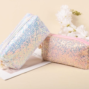 May include: Two sparkly cosmetic bags, one white and one pink, with a zipper closure. Both bags are covered in iridescent sequins.