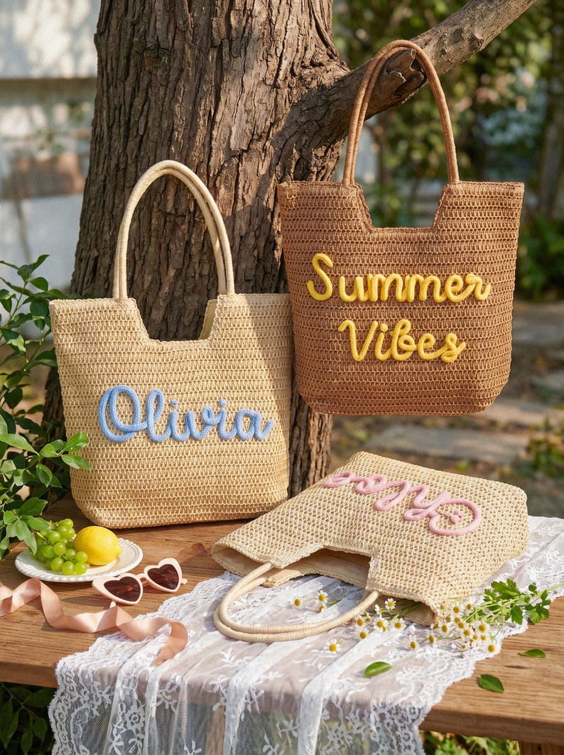 May include: Three woven straw tote bags with two handles each. One light beige bag features the blue text Olivia, one brown bag features the yellow text Summer Vibes, and one light beige bag features the pink text Chloe in cursive script.