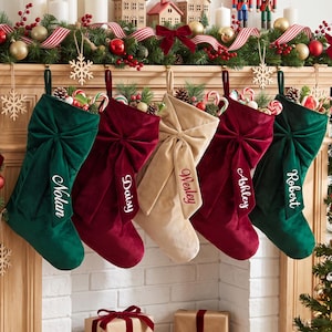 May include: Five velvet Christmas stockings hanging in a row, featuring large bows and personalized names: Nolan, Daisy, Wesley, Ashley, and Robert. The stockings are colored in dark green, deep red, and beige, each filled with candy canes and pine.